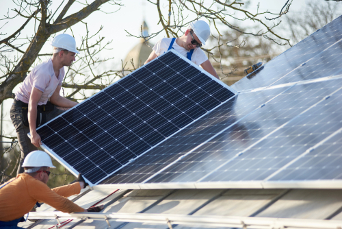 Three men engaged in the installation of a solar panel on a rooftop, contributing to eco-friendly energy initiatives.