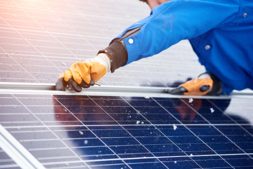 A man in blue overalls works diligently on a solar panel, contributing to renewable energy efforts.