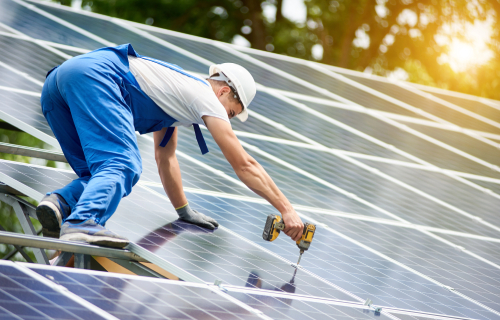 A man in blue overalls adjusts solar panels on a roof, focusing on renewable energy installation.