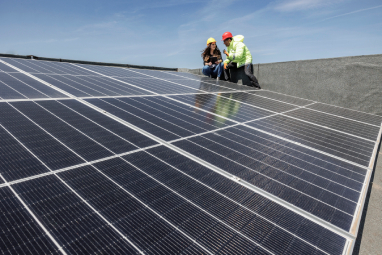 Two men are engaged in the installation of a solar panel on a rooftop, highlighting sustainable energy practices.