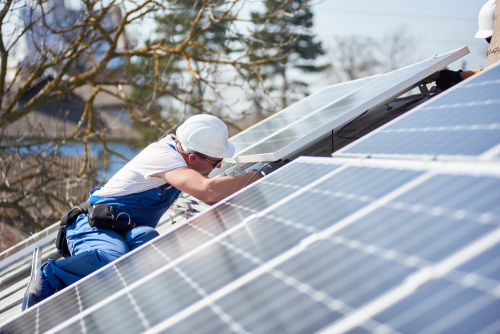 A man wearing blue overalls is engaged in the installation of a solar panel, demonstrating renewable energy efforts.