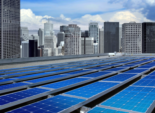Solar panels installed on a building roof with a city skyline visible in the background.