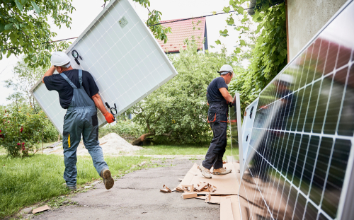 Two men are collaborating to install a solar panel, demonstrating teamwork and technical skills on a sunny day.