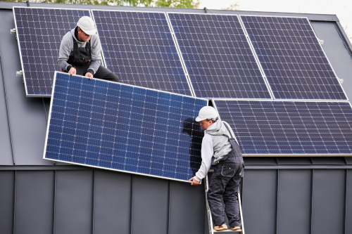 Two men collaborating on a rooftop, installing solar panels with tools and equipment nearby.