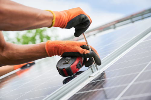 A man in orange gloves operates a tool to cut solar panels, demonstrating solar panel installation work.